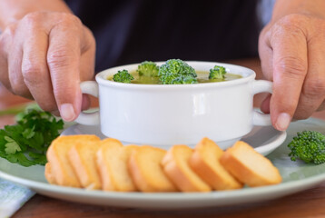 Two female hands holding a white bowl filled with a broccoli cream soup. Vegan vegetarian concept