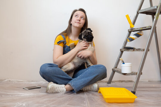 Independent young woman with pug dog planning renovation apartment sitting on floor with construction tool. diy repair owner hands with pet 