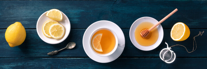 A cup of lemon tea and honey panorama on a dark rustic wooden background. Healthy organic citrus...