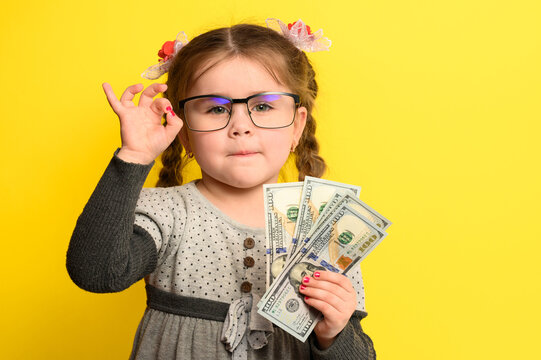 Money and children on the background, a rich girl with glasses holding a large sum of money.