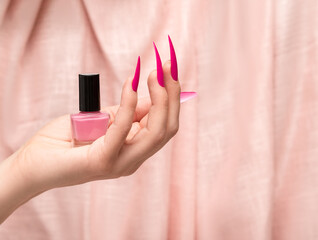 Female hand with pink stiletto nail design. Long nail polish manicure. Woman hand holding pink nail...