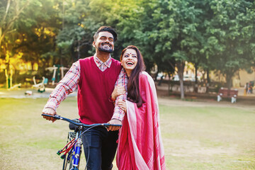 Young Indian couple in traditional ethnic clothes walking with the bicycle in the park