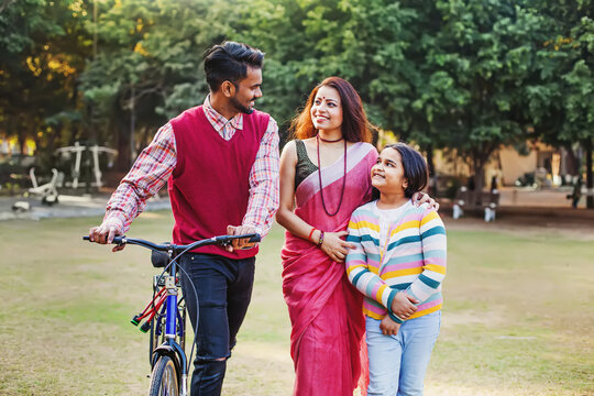 Beautiful Indian Family With Little 10-year-old Daughter Walking With Bicycle Outdoors In A Park