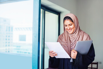 Beautiful arabic Muslim young woman in hijab holding laptop in a city - obrazy, fototapety, plakaty