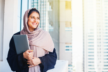 Beautiful arabic Muslim young woman in hijab holding laptop in a city