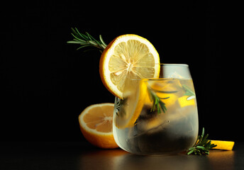 Cocktail gin-tonic with lemon slices and twigs of rosemary on a black background.
