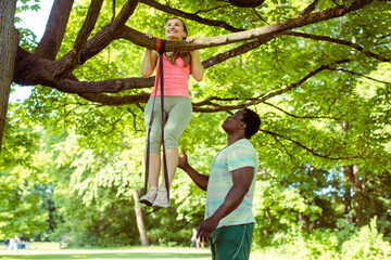 Woman doing pull-up assisted by her fitness coach on tree