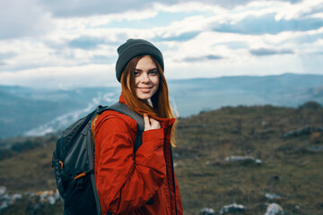 Naklejka premium happy woman in a red jacket with a backpack and in a hat mountains in the background fresh air