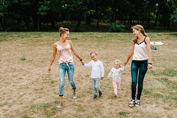 Two mothers with kids walking on nature on summer day. Mom and son, daughter walk in the park. Concept of happy family. Close Up.