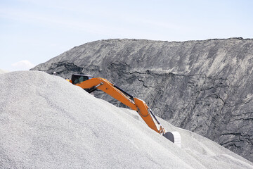 Industry, excavator tractor with a bucket works on top of a pile of gravel at an asphalt plant at a...