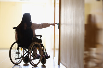 Woman in wheelchair reaches out to open handle of door in dark hallway