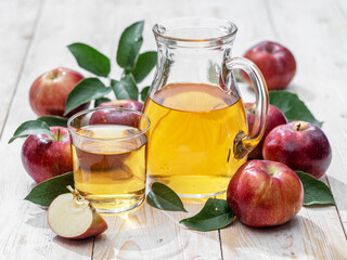 Glass of juice and carafe of fresh apple juice and organic apples on wooden table.
