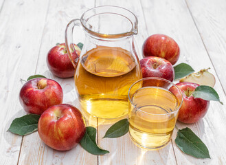 Glass of juice and carafe of fresh apple juice and organic apples on wooden table.