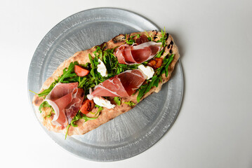 Sandwich with prosciutto, cheese and fresh arugula served on a metal tray over white background.