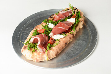 Sandwich with prosciutto, cheese and fresh arugula served on a metal tray over white background.