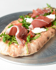 Sandwich with prosciutto, cheese and fresh arugula served on a metal tray over white background.