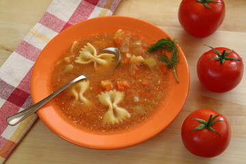 tomato soup in a bowl on table, decorated with green herbs, three ripen tomatoes and linen kitchen cloth next to, top view
