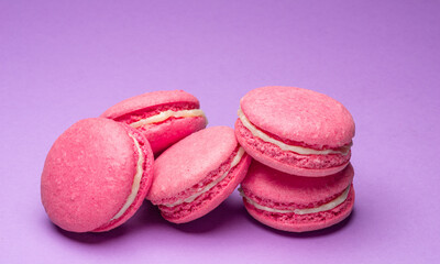 Colorful sweet macarons or macaroons, flavored cookies on purple background.