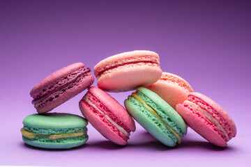 Colorful sweet macarons or macaroons, flavored cookies on purple background.