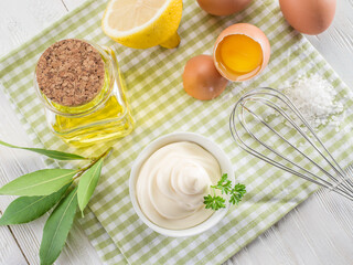 Bowl with mayonnaise sauce in the centre and mayonnaise ingredients around it on wooden table. Top view.