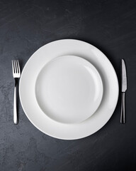 Place setting with high-gloss plate, knife fork. Isolated on black, set table.