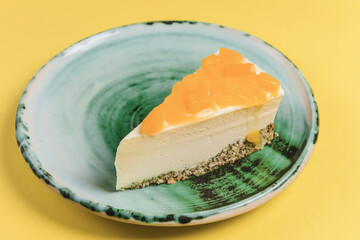 Fresh mango cheesecake served on a blue plate over yellow background.