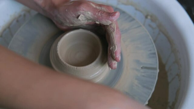 Female potter hands working with clay in workshop. White desk on background