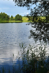 Beautiful summer sunny landscape with a calm big river, trees and wooded banks on the other side. Blue sky with clouds reflected in the water. No people