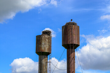 Two old rusty metal water towers in the village. Storks nests on top of a Russian water tower