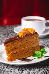 One piece of chocolate honey cake served on a white plate with a cup of tea over blurred background.