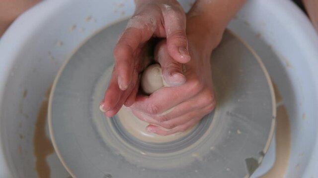 Female potter hands working with clay in workshop. White desk on background