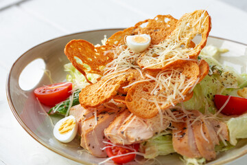 Caesar salad with grilled chicken on white wooden background