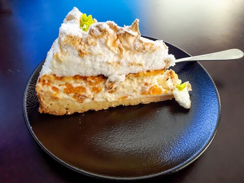 Triangular piece of dessert cake with cream, cottage cheese and pieces of peaches, meringue and decorated with caster sugar