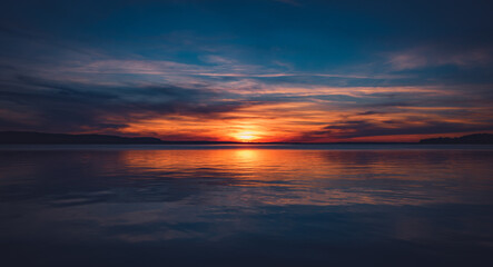 Ein Panorama Blick ins Jenseits an einem wunderschönen Sonnenuntergang mit kräftigen Farben bei spiegelglattem See im Hochsommer - obrazy, fototapety, plakaty