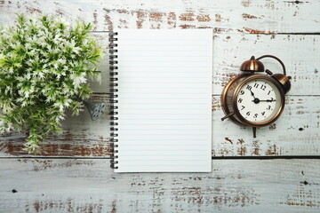 Notebook with blank pages withh alarm clock and floweron wooden background