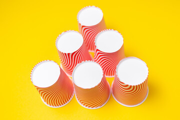 A pyramid of striped red paper cups, on a yellow background. Top view. Close up