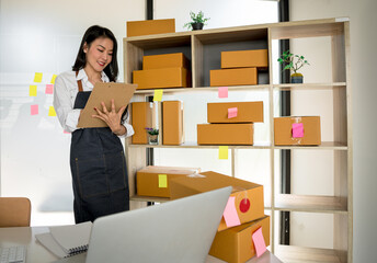 Young smiling beautiful owner asian woman freelance sme business online shopping working on laptop computer with parcel box at home - SME business online and delivery concept
