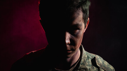 Portrait of a close-up of a soldier in scars and battle paint, half-lit against the backdrop of red...