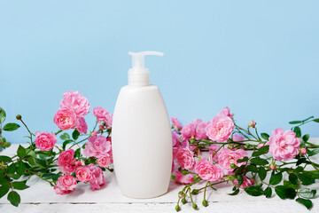 bottle with shampoo or shower gel and pink flowers roses on blue background, body care and beauty products