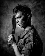 Black white portrait of a young soldier in combat coloring, scars and bruises, holding a machete on...