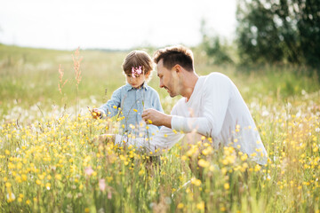 Fototapeta premium Young dad spending time with his little son in nature, collecting bouquet for mom from wildflowers, fathers day