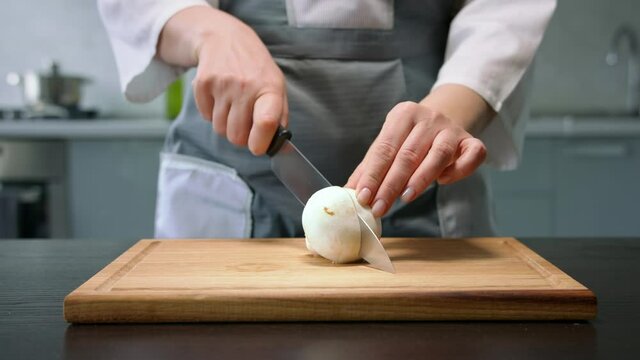 Female hands cut whole champignon mushroom into halves by knife on wooden board