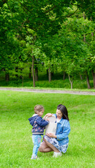 Fototapeta premium Mom and little daughter holding a gift box with the inscription Be happy close up without a face. Mother with baby outside