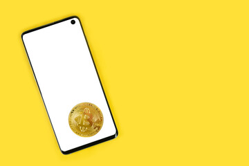 Smartphone with blank white mockup on screen and Bitcoin cryptocurrency coin on top, isolated on yellow background with copy space. Template for crypto exchanche, investing app