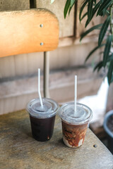 Close up of take away plastic cup of iced black coffee (Americano) and iced coffee latte on wooden table in garden with copy sapce.