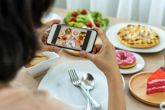A reviewer's hand using a mobile phone to take pictures of food at a restaurant table.Take photo to write a review of the restaurant to share on the internet.