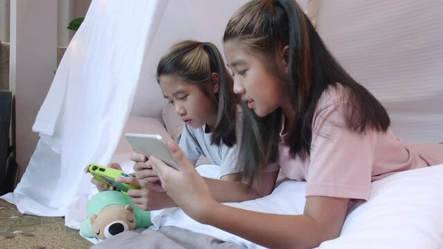 4K Kid play portable game together in bed sheet tent. Two girl sibling happy enjoy and fun to play portable game together. Sibling girl play game in bed sheet tent at home