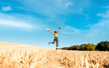 Happy woman jumping on golden wheat in summer time - Happiness concept with young girl raising arms up to the sky - Travel and success concept