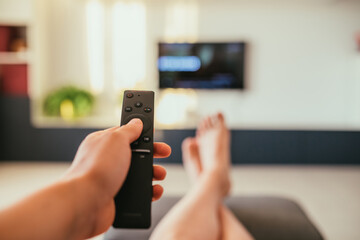 Selective focus image with a remote control and relaxing feet and tv in a modern living room. 