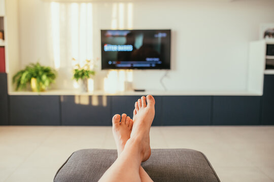 Selective focus image of relaxing feet and tv in a modern living room with natural sunset lights. 